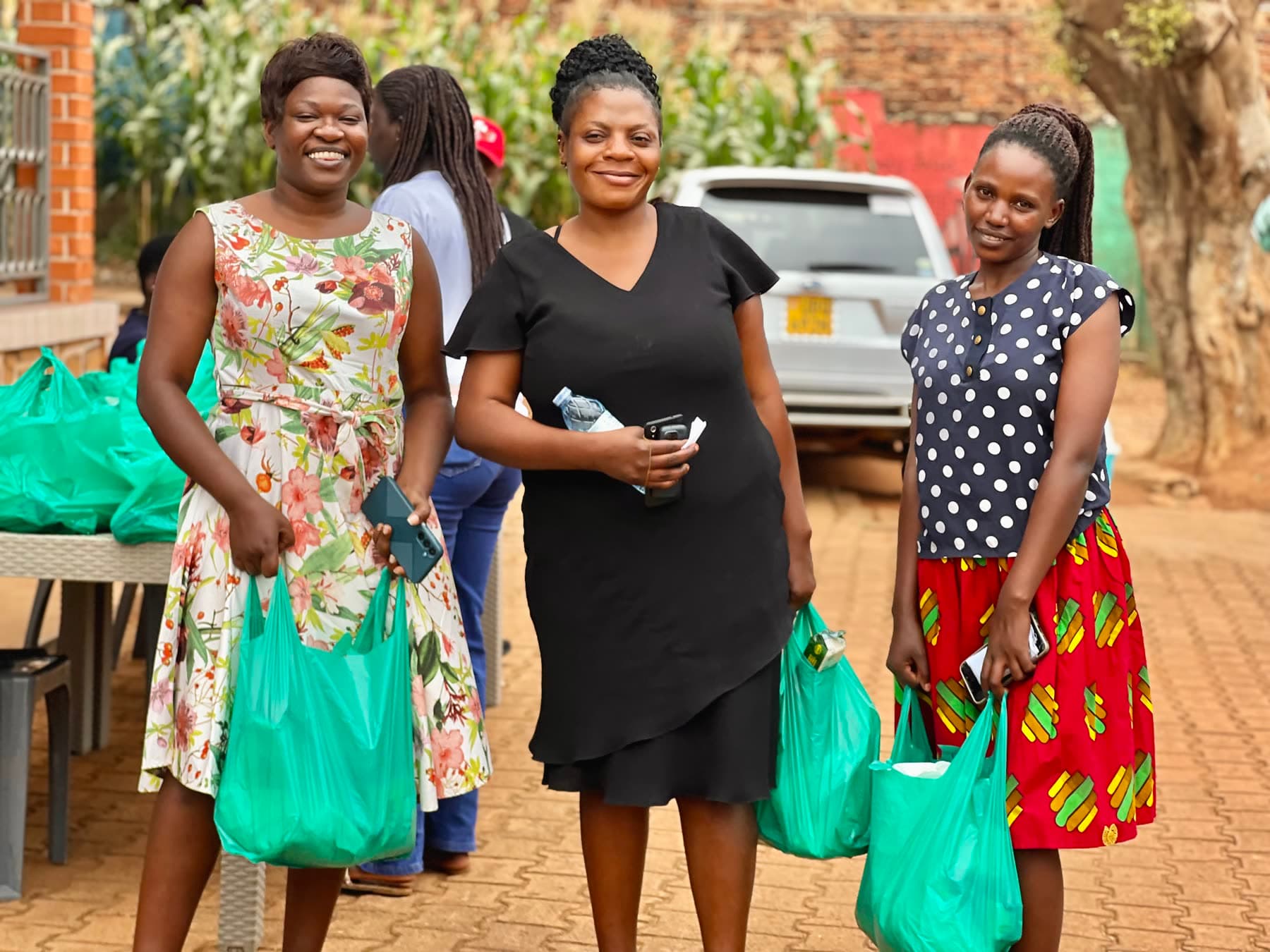 Three women smiling with their Healthy Steps food packages in Wakiso