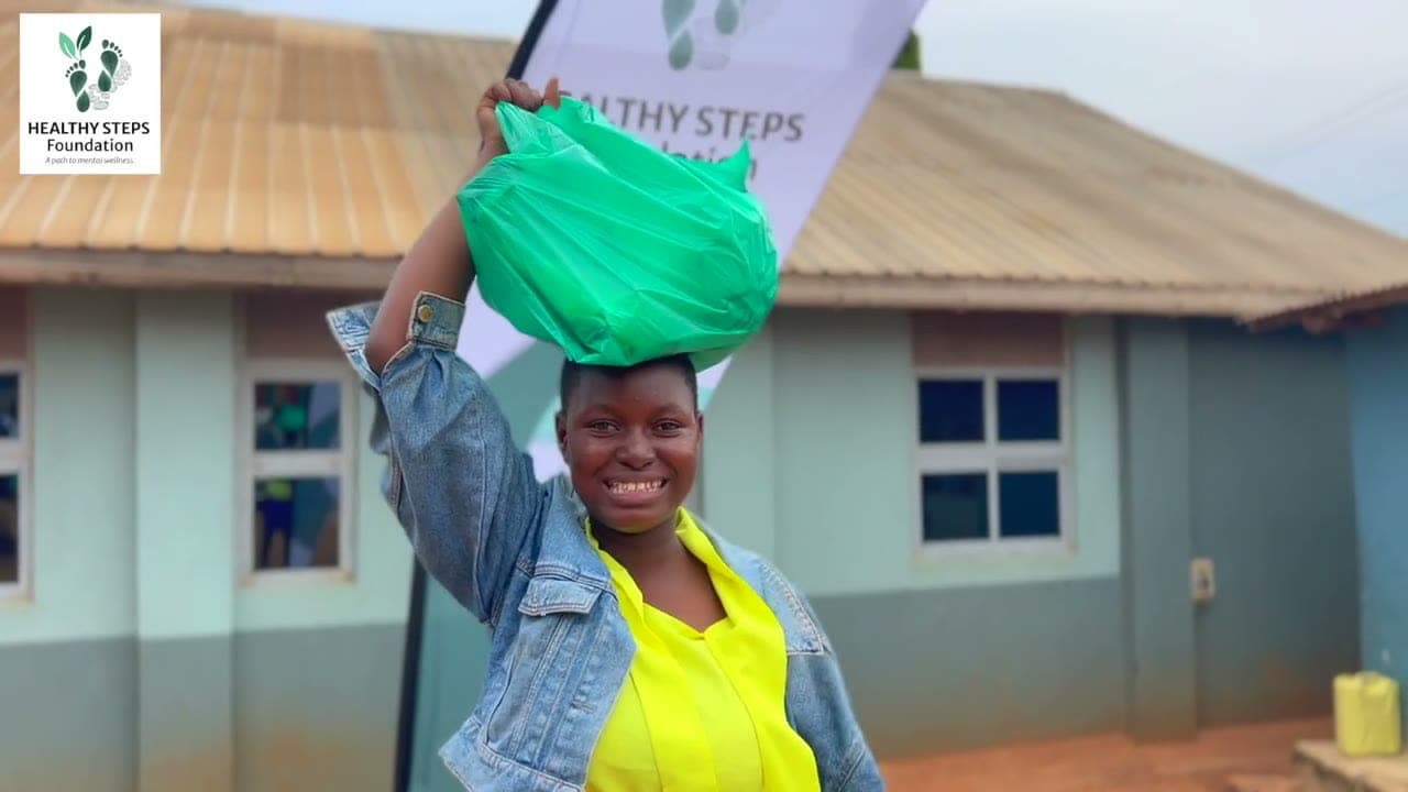 A young woman smiling as she carries a Healthy Steps Foundation food package during the June outreach in Wakiso, Uganda